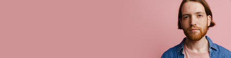 Young ginger man with beard posing and looking at camera isolated over pink backgroundの写真素材