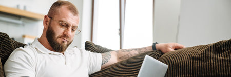 White man with prosthesis writing down notes and using laptop while siting on couch at homeの写真素材