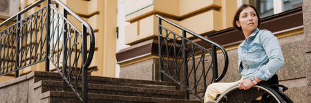 Brunette woman sitting in wheelchair by stairs on city streetの写真素材