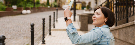 Brunette woman taking selfie on mobile phone while sitting in wheelchair at city streetの写真素材