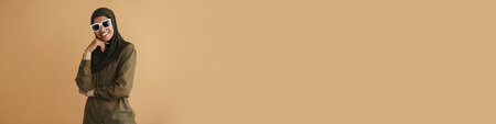 Black muslim woman in hijab smiling and looking at camera isolated over beige background