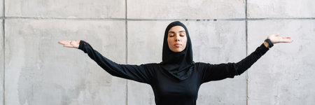 Young muslim woman in hijab meditating while sitting on fitness mat indoors