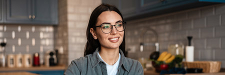 White smiling woman writing down notes while working with laptop at home kitchenの写真素材