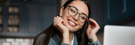 White smiling woman in eyeglasses working with laptop at home kitchenの写真素材