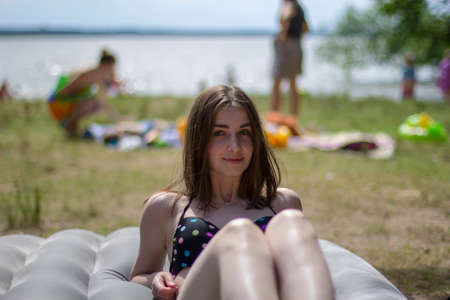 A young girl in a swimsuit sunbathes on the seashore on an air mattress