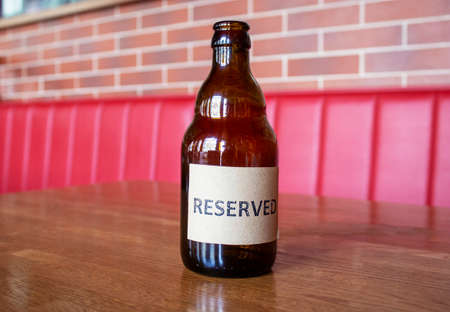 A glass bottle on a wooden table in a restaurant with the inscription Reserved.の写真素材