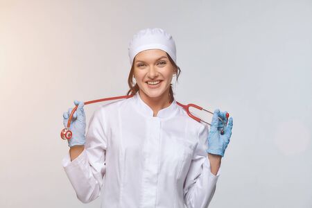 Medical concept of a female doctor in a white coat with a stethoscope, doctor. A female hospital worker looks at the camera and smiles, Studio, White backgroundの写真素材