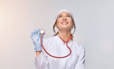 Medical concept of a female doctor in a white coat with a stethoscope, doctor. A female hospital worker looks at the camera and smiles, Studio, White backgroundの写真素材