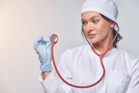 Medical concept of a female doctor in a white coat with a stethoscope, doctor. A female hospital worker looks at the camera and smiles, Studio, White backgroundの写真素材
