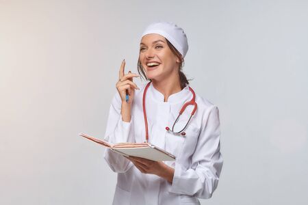 Medical concept of a female doctor in a white coat with a stethoscope, doctor. A female hospital worker looks at the camera and smiles, Studio, White backgroundの写真素材