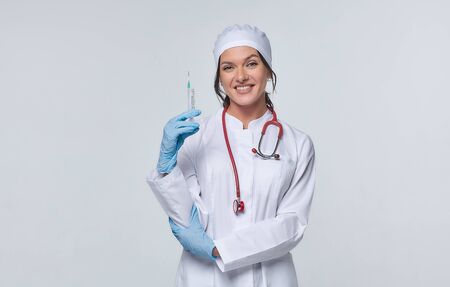 Medical concept of a female doctor in a white coat with a stethoscope, doctor. A female hospital worker looks at the camera and smiles, Studio, White backgroundの写真素材