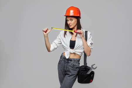 a girl in an orange construction helmet with a measuring tape and a bag, depicting a worker on a white background ..の写真素材