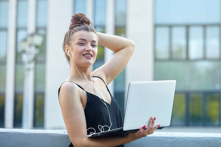 beautiful girl walks around the city, working on a laptop. holding a laptop and listening to music.の写真素材