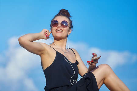 beautiful girl poses in the city, holding a smartphone and listening to music with headphones.の写真素材