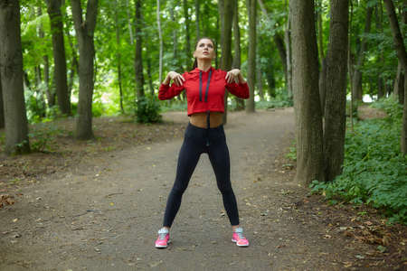 girl in a mask and sportswear does gymnastic exercises on the grass in a city park.