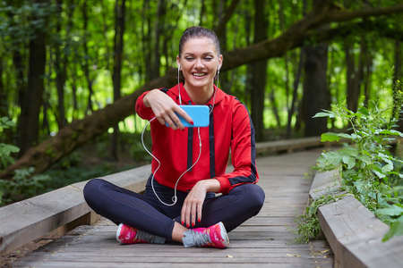 Distance learning concept. An attractive girl in sportswear sits on a wooden path in a forest park....