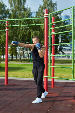 athletic man, in the morning in the city Park doing exercises with gymnastic ropes
