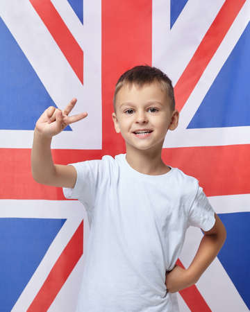 the cute boy folded his fingers in the shape of a V against the background of the British flagの写真素材