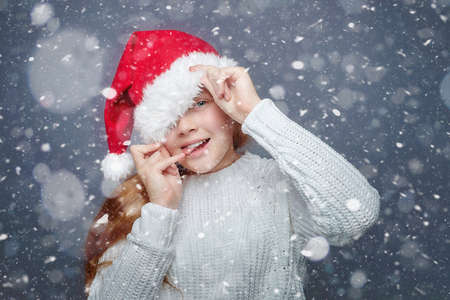 attractive red-haired teenage girl in a Santa hat. The concept of Christmas and the New year. photo session in the Studio on a white backgroundの写真素材