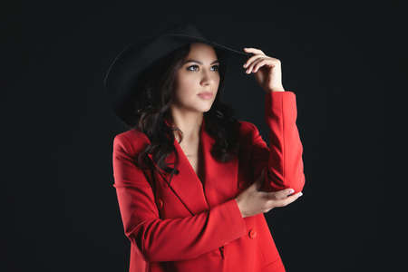 portrait of an attractive woman in a red jacket and a hat with a large brim. photo shoot in the studio on a dark backgroundの写真素材