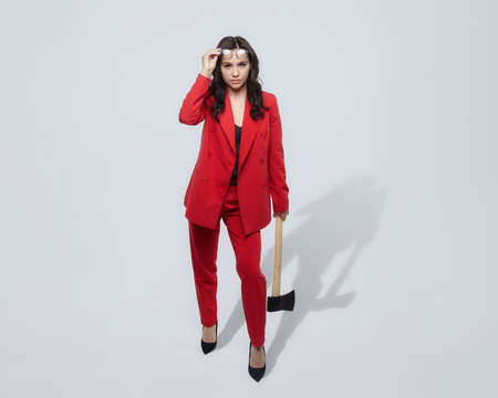 attractive woman in a red suit and carrying an ax. the concept of a serious business womanの写真素材