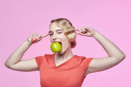 attractive young blonde with a retro hairstyle holds a green apple near her faceの写真素材