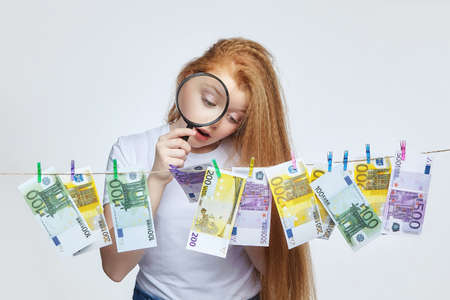 attractive red-haired girl holds 100-dollar and euro banknotes near her faceの写真素材