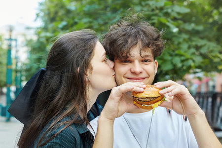 young girl holds a hamburger in her hands in front of her face.の写真素材