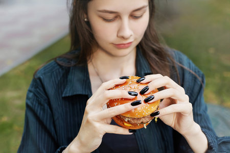 young girl holds a hamburger in her hands in front of her face.の写真素材