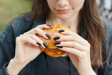young brunette holds a hamburger in her hands and bites French fries.の写真素材