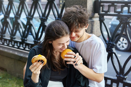 guy and a girl are holding burgers and drinks in their hands. the girl gives the guy a drink from her glass.の写真素材