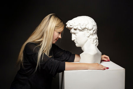 attractive blonde posing with a bust of David. photo shoot in the studio on a black background.の写真素材