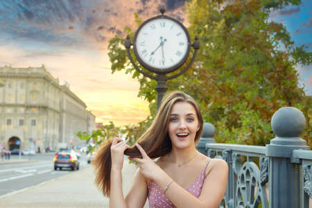 cute girl with long hair is standing in the city near a large clock ..