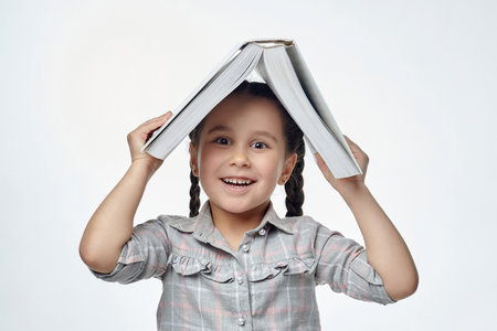 little black-haired girl holds a red book in her hands and points to the free space with her index finger.の写真素材