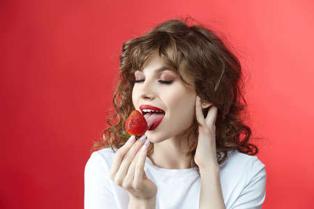 attractive girl with a smile holds a strawberry in her hands. photo shoot in the studio on a white backgroundの写真素材