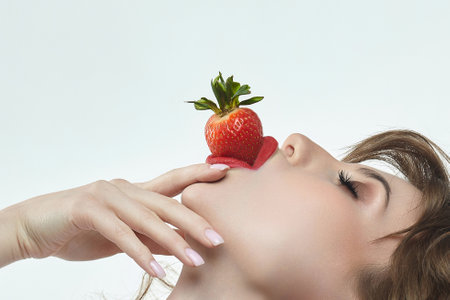 attractive girl with a smile holds a strawberry in her hands. photo shoot in the studio on a white backgroundの写真素材