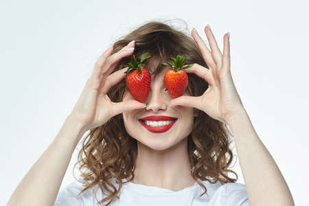 attractive girl with a smile holds a strawberry in her hands. photo shoot in the studio on a white backgroundの写真素材