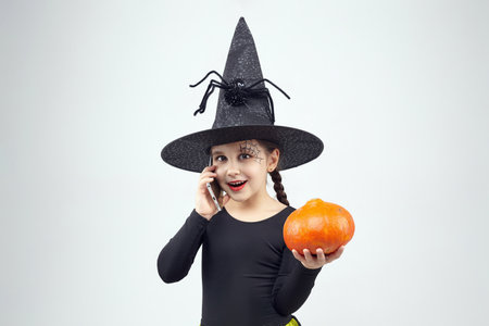 charming little girl in a witch costume is talking on her smartphone. the concept of the Halloween holiday.の写真素材