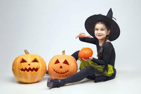 charming little girl in a witch costume is talking on her smartphone and holding a magic book. There are Jack's lamps around.の写真素材