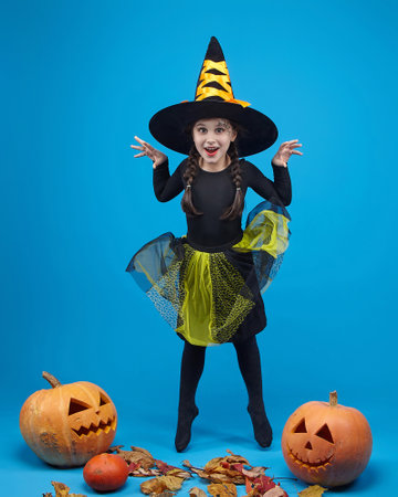 charming little girl in a witch costume dancing in the studio on a blue background.の写真素材