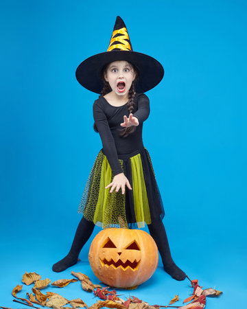 charming little girl in a witch costume dancing in the studio on a blue background.の写真素材