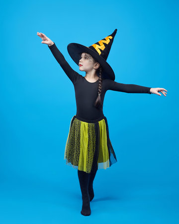 charming little girl in a witch costume dancing in the studio on a blue background.の写真素材