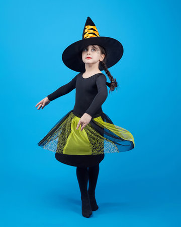 charming little girl in a witch costume dancing in the studio on a blue background.の写真素材