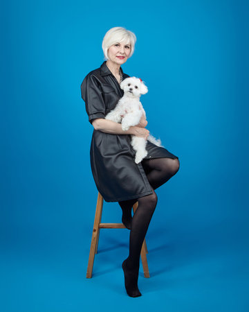 portrait of an adult blonde with a small Maltese lapdog on a blue background.の写真素材