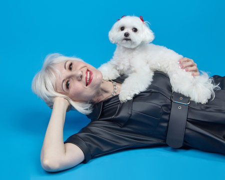 portrait of an adult blonde with a small Maltese lapdog on a blue background.の写真素材