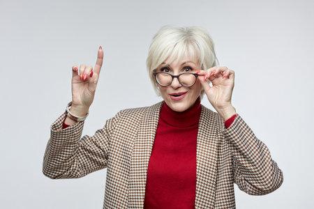beautiful elderly woman with glasses shows her index finger up. advertising concept of a business...
