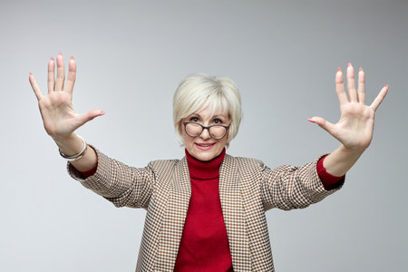 beautiful elderly woman with glasses holds her hands in front of her with open palms facing the camera. advertising concept of a business woman leader.の写真素材