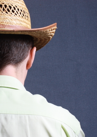shoulder portrait of a man standing with his back to the camera with a straw hat on his head, on a gray backgroundの写真素材