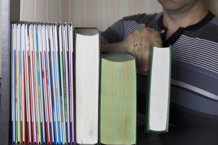 The man in the library takes a book off the shelf. View from the bottom of the bookcase. Choosing books to read.の写真素材