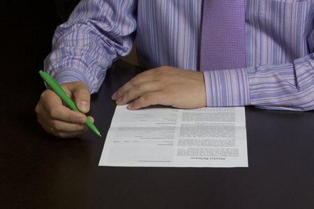 A man reads a model release before signing it. On the table lies a dark pure form. The hand holds a pen to fill out and sign.の写真素材